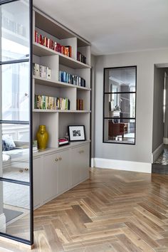 a living room filled with lots of books on top of wooden flooring next to a window