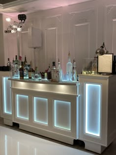 a white bar with several bottles on it and lights behind the bar area in front of them