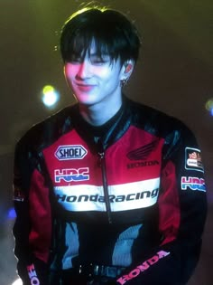 a young man wearing a red and black jacket standing in front of a stage with lights behind him