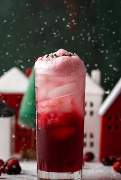 a red drink with whipped cream and sprinkles on the rim in front of small houses