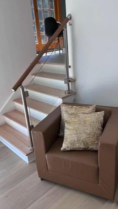 a brown chair sitting in front of a stair case with a pillow on it's back