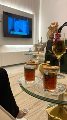 two glasses of wine are sitting on a glass table in front of a flat screen tv