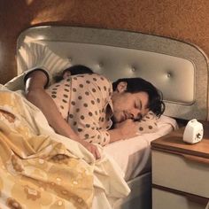 a woman laying in bed with her head on the pillow next to a night stand