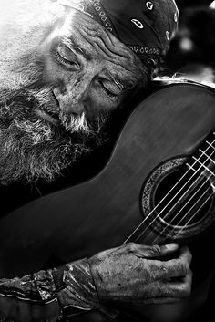 an old man with a beard playing the guitar in black and white photo by john moore