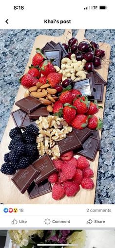 a wooden cutting board topped with chocolate covered strawberries and almonds next to a vase filled with flowers