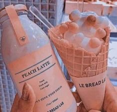 a hand holding an ice cream cone with peaches in it and a bottle of liquid next to it