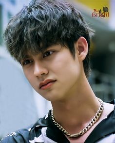 a young man with black hair and a necklace on his neck looking at the camera