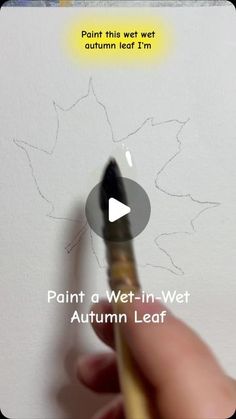 a person holding a paintbrush in their left hand and drawing on the wall with an autumn leaf