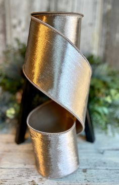 a silver vase with a ribbon wrapped around it on top of a wooden table next to greenery