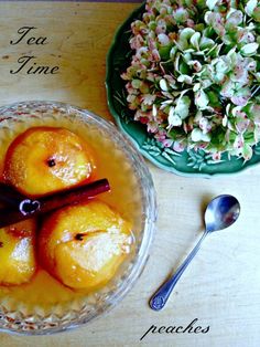 a bowl filled with peaches on top of a wooden table next to a vase and spoon