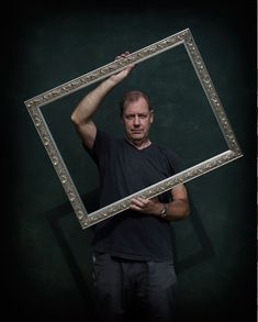 a man holding up a framed photo in front of his face with one hand and the other