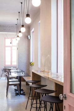 an empty restaurant with tables and stools next to the bar area that has several lights hanging from the ceiling