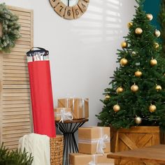 a christmas tree with presents under it in front of a clock on the wall next to a wooden table