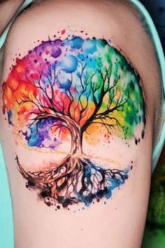 a colorful tree tattoo on the back of a woman's thigh with watercolors