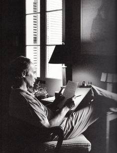 a man sitting in a chair reading a book next to a lamp on a desk