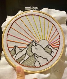 someone is holding up a hand embroidery project with mountains and sun in the sky on it