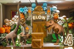 two dinosaurs are standing in front of an entrance to a birthday party with balloons and decorations