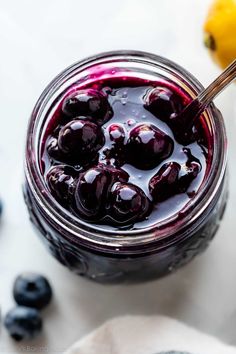 a jar filled with blueberry jam next to fresh blueberries on a white surface