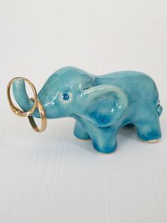 an elephant figurine with two rings attached to it's trunk on a white surface