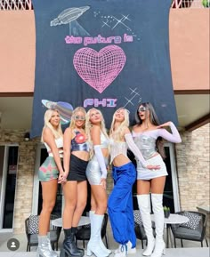 four beautiful young women standing next to each other in front of a black and white sign