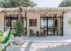 two wooden chairs sitting in front of a thatched roof house with glass doors and windows