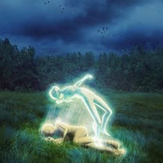 a person laying in the grass with a light up figure on their back and trees in the background