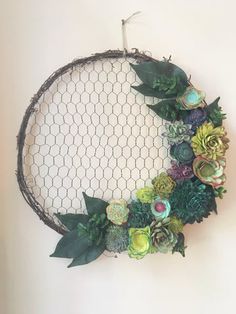 a wire wreath with succulents and greenery hanging from the side on a wall