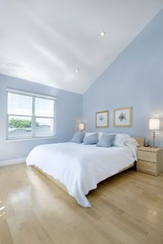 a bedroom with light blue walls and white bedding, hardwood flooring and two windows