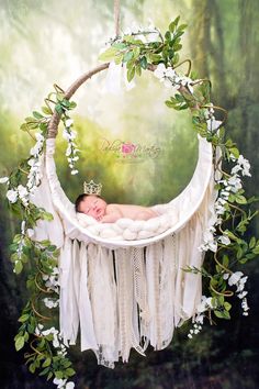 a baby is sleeping in a white hammock surrounded by greenery and flowers