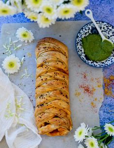 a pastry on a tray next to some flowers and a bowl with pesto in it