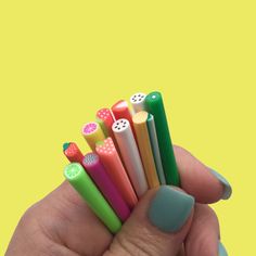 a person holding six different colored pens in their hand and one has a green nail