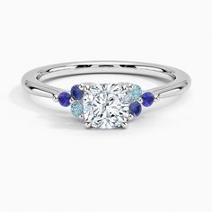 a diamond and blue sapphire engagement ring with three stones on the band, set in white gold