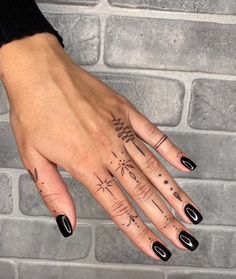 a woman's hand with black nail polish and tattoos on her left hand, next to a brick wall