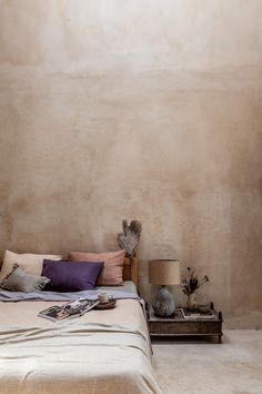 a bed sitting in a bedroom next to a lamp on a wooden table and two vases