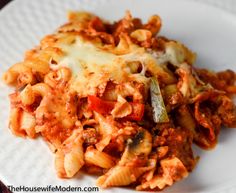 a white plate topped with pasta covered in sauce and cheese, on top of a wooden table