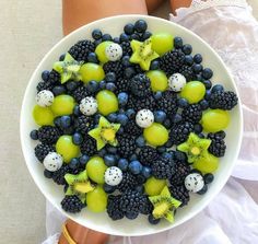 a white bowl filled with grapes, kiwis and blackberries on top of a woman's legs