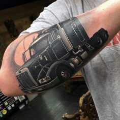 a man's arm with a black and grey truck tattoo on the left arm