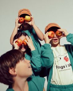 three children are holding apples in front of their eyes and looking at the same person