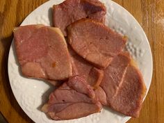 slices of ham on a white plate sitting on a wooden table