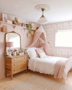 a bedroom decorated in pink and white with a canopy over the bed, dresser and mirror