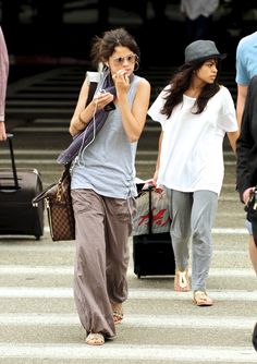 two women walking down the street while using their cell phones and carrying suitcases behind them