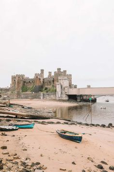 two small boats on the beach near a bridge and water way with castle ruins in the background