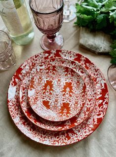 red and white dinner plates on a table with glasses, napkins and greenery