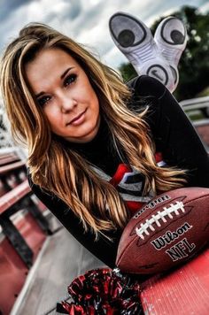 a woman holding a football in her right hand and posing for a photo on the sidelines