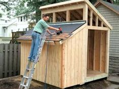 a man standing on top of a ladder next to a wooden shed with a roof