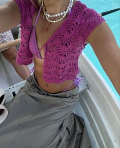 a woman sitting in a boat wearing a purple top and pearls on her necklaces