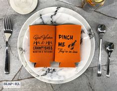 two orange napkins sitting on top of a white plate next to silver utensils