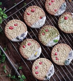 six cookies with frosting and sprinkles are on a cooling rack next to green leaves