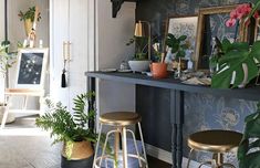 a room filled with lots of plants and pictures on top of a shelf next to two stools