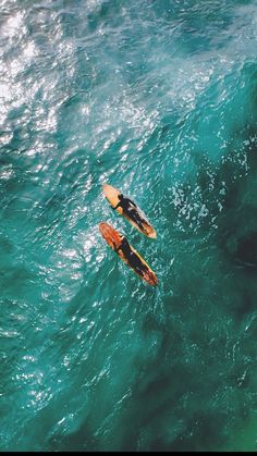 two people on surfboards in the middle of an ocean with green water and blue sky